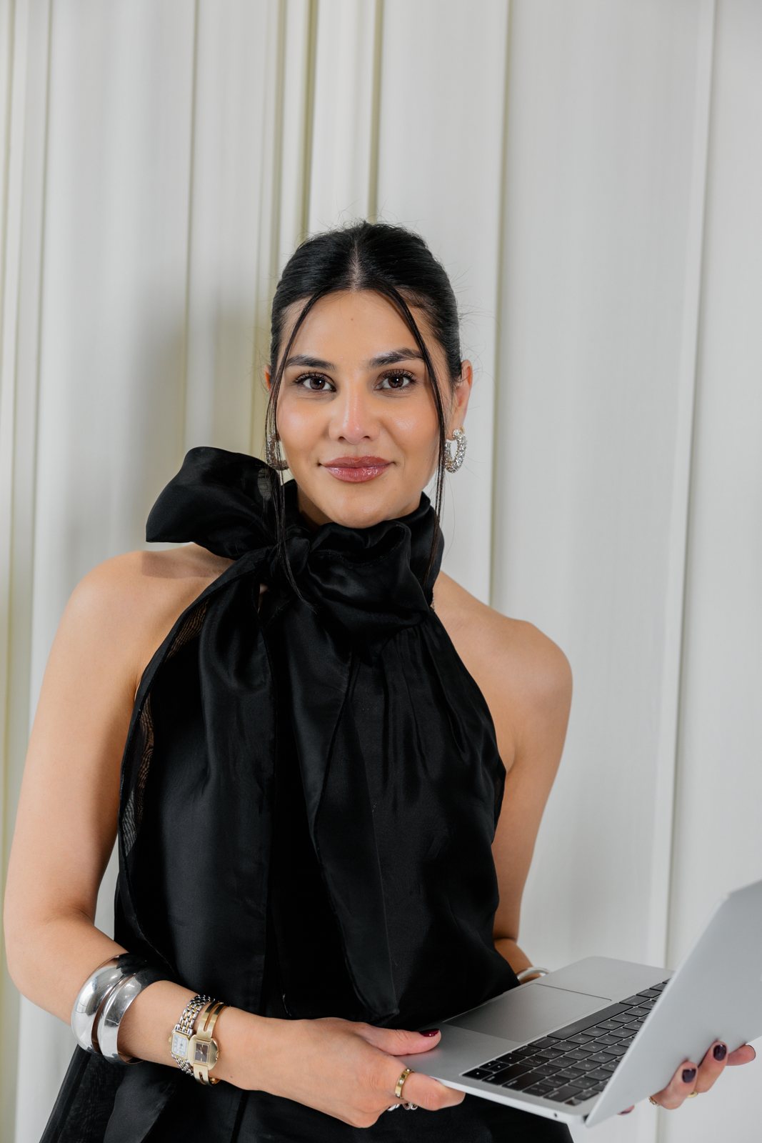 Camila Luna seated with her laptop in a black bow-neck top