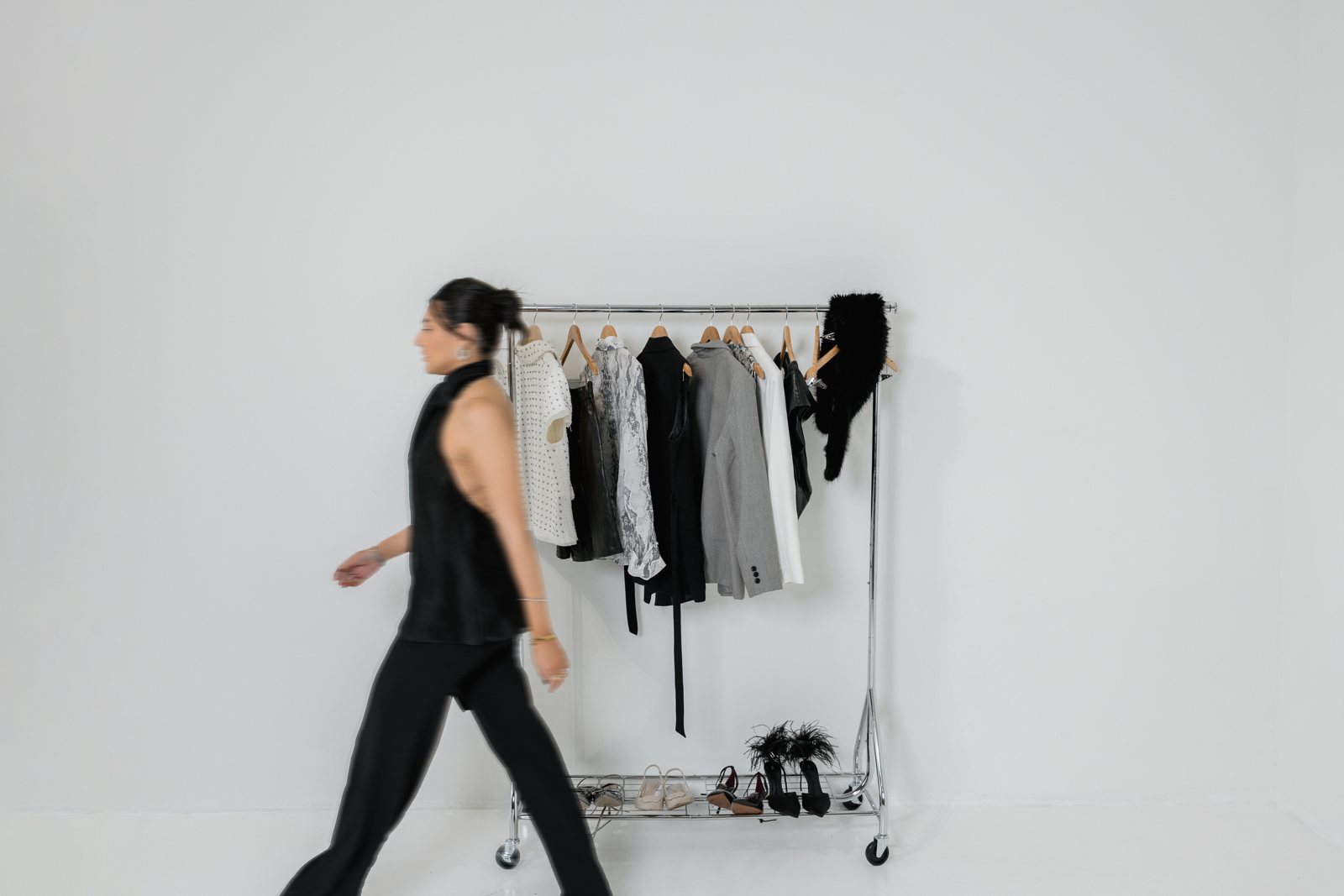 Camila Luna walking past a rack of curated pieces in a black halter top and wide-leg trousers